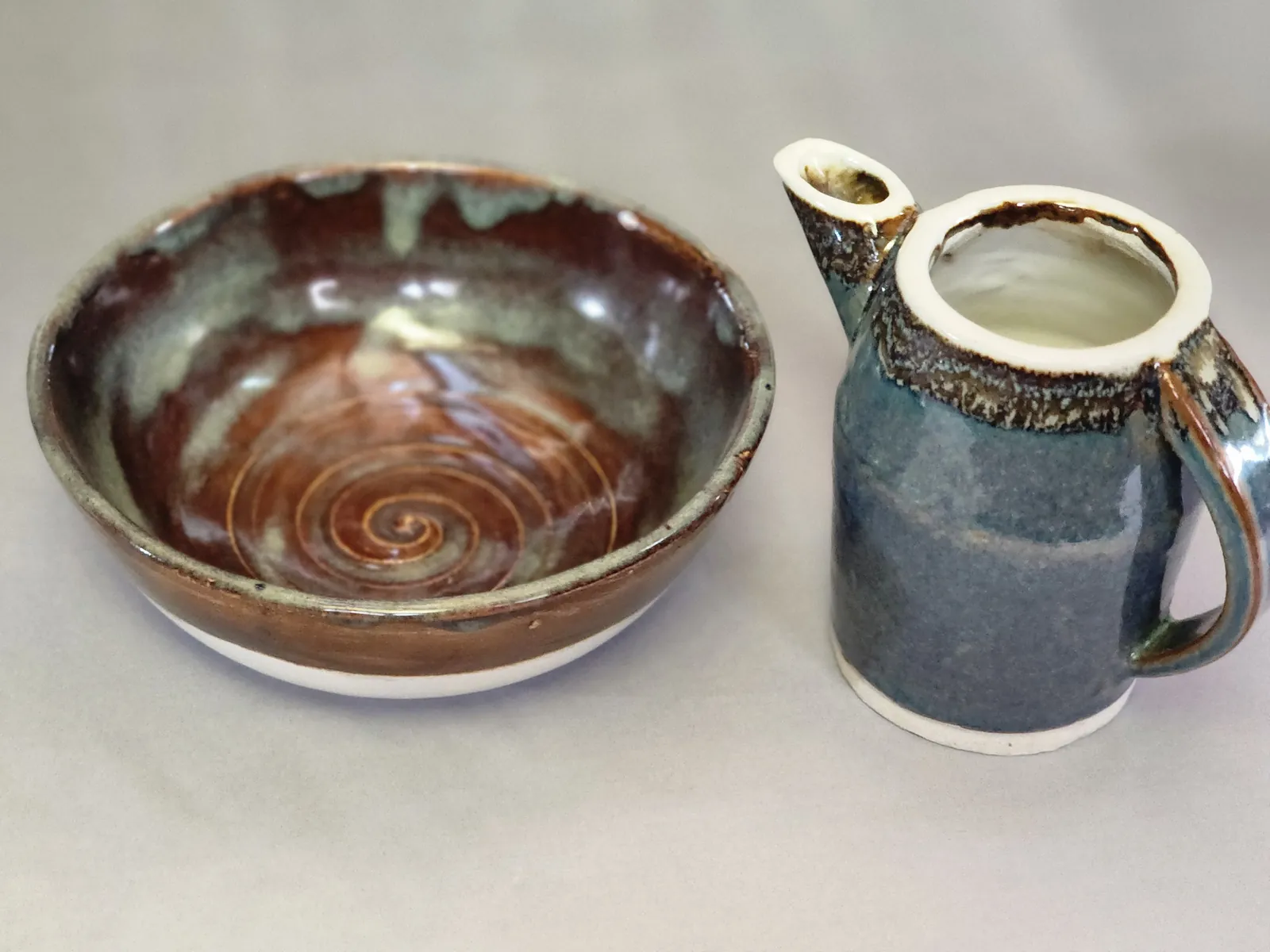 A glazed spiral bowl beside a blue and brown pitcher